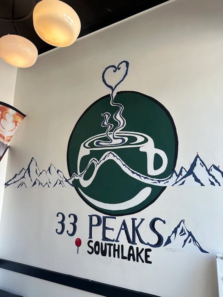 Hand-painted 33 Peaks Southlake wall mural — a green coffee-cup logo with steam curling into a heart above a mountain range